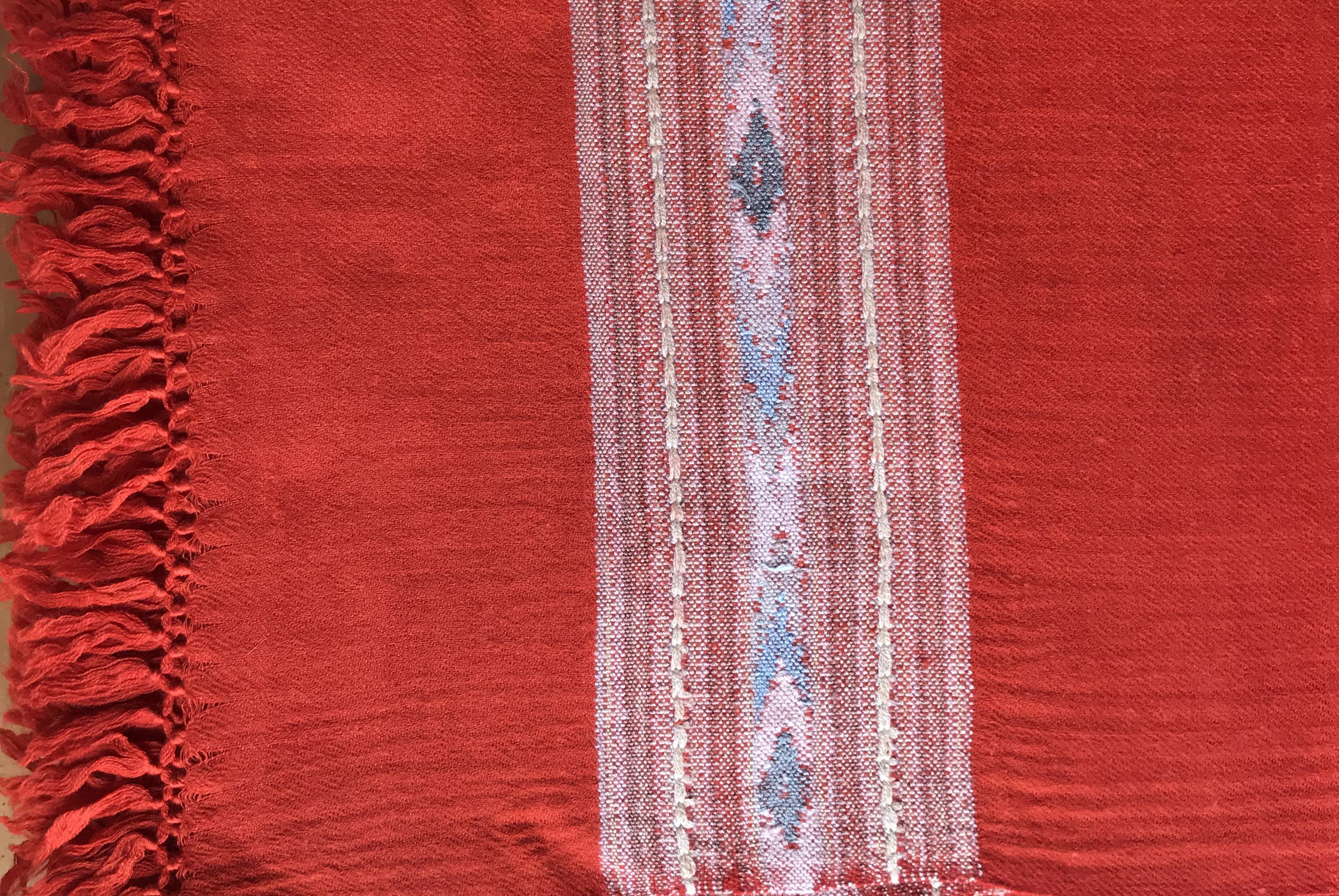 Close-up of a red shawl with fringe, highlighting the intricate woven design in contrasting colors.