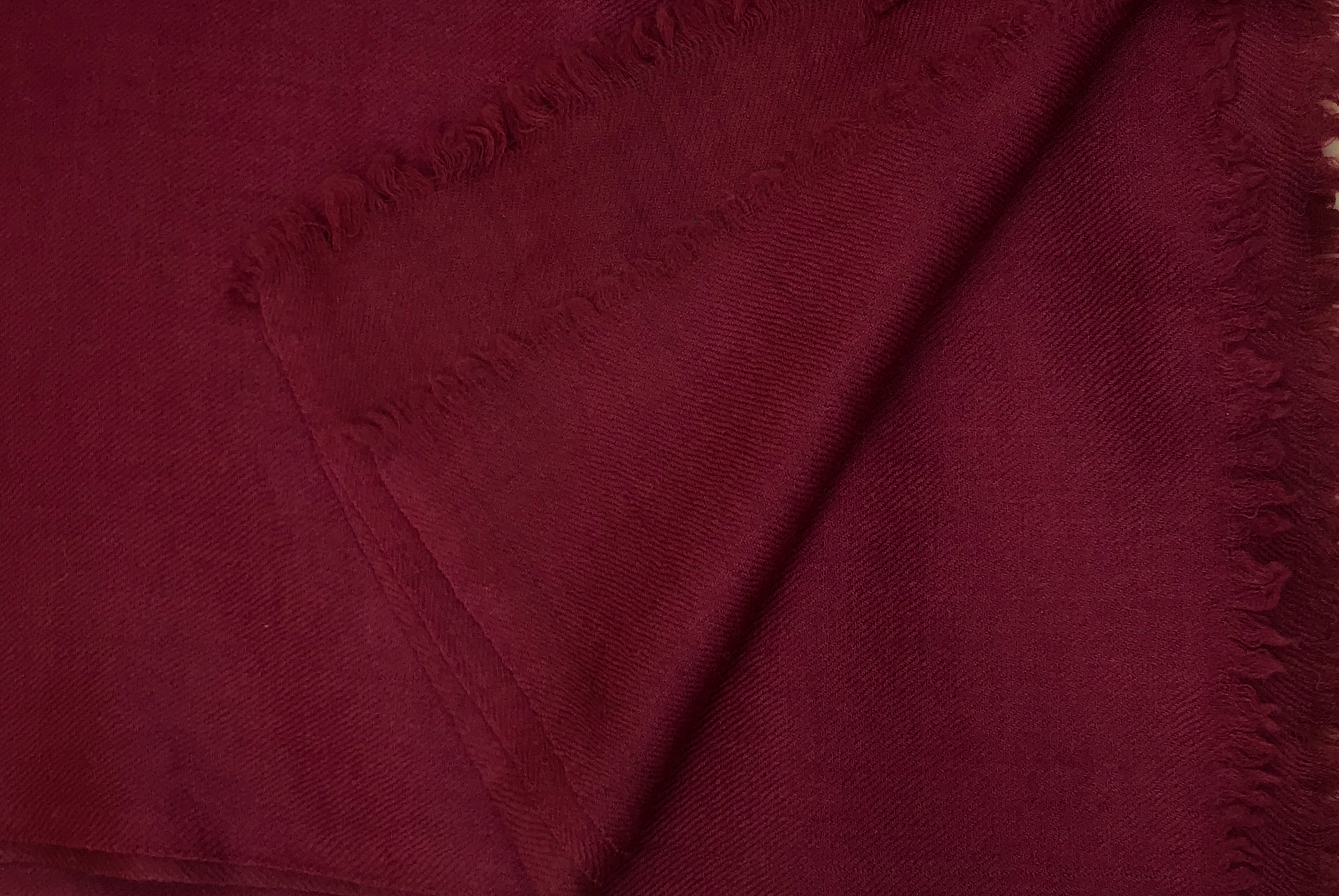 The image highlights the intricate texture and fine weave of a Shambhala large burgundy wool shawl. The rich burgundy color, complemented by its soft and delicate fringes, showcases its luxurious quality.