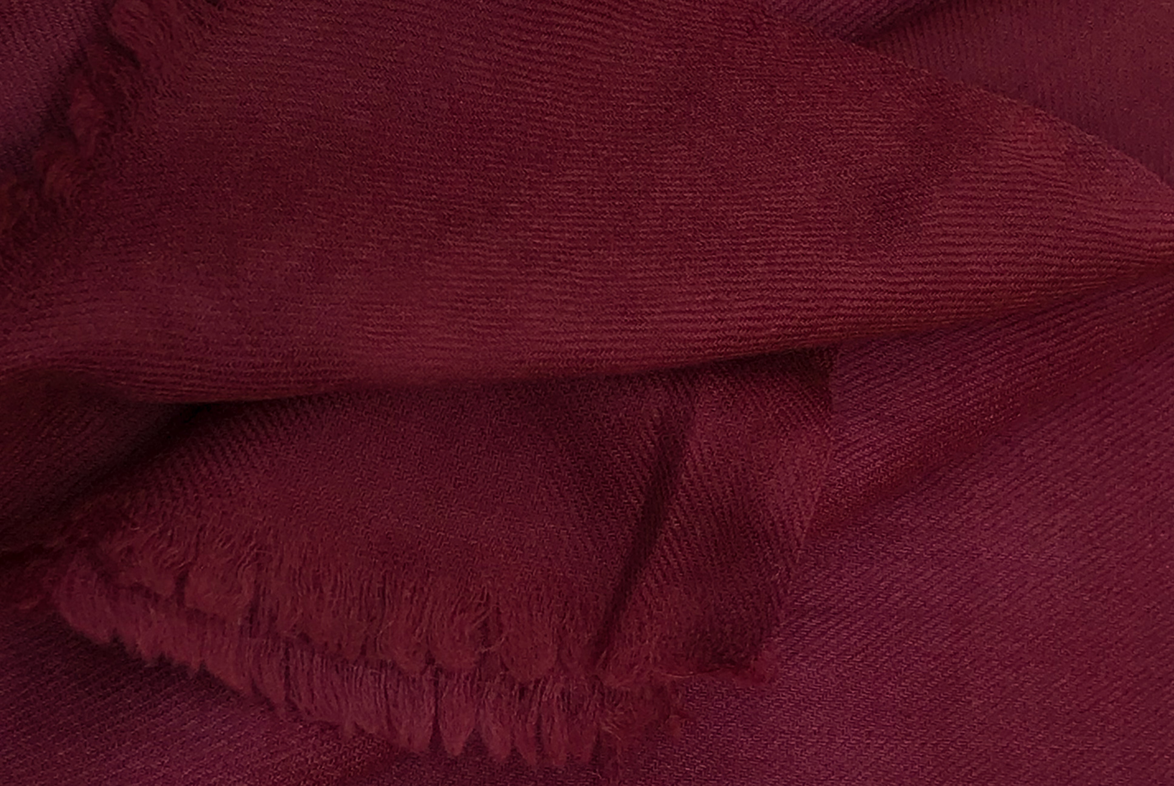 A close-up of a burgundy wool shawl from Esprit de l'Himalaya, showcasing its soft and warm texture with delicate fringes, ideal for meditation and winter wear.