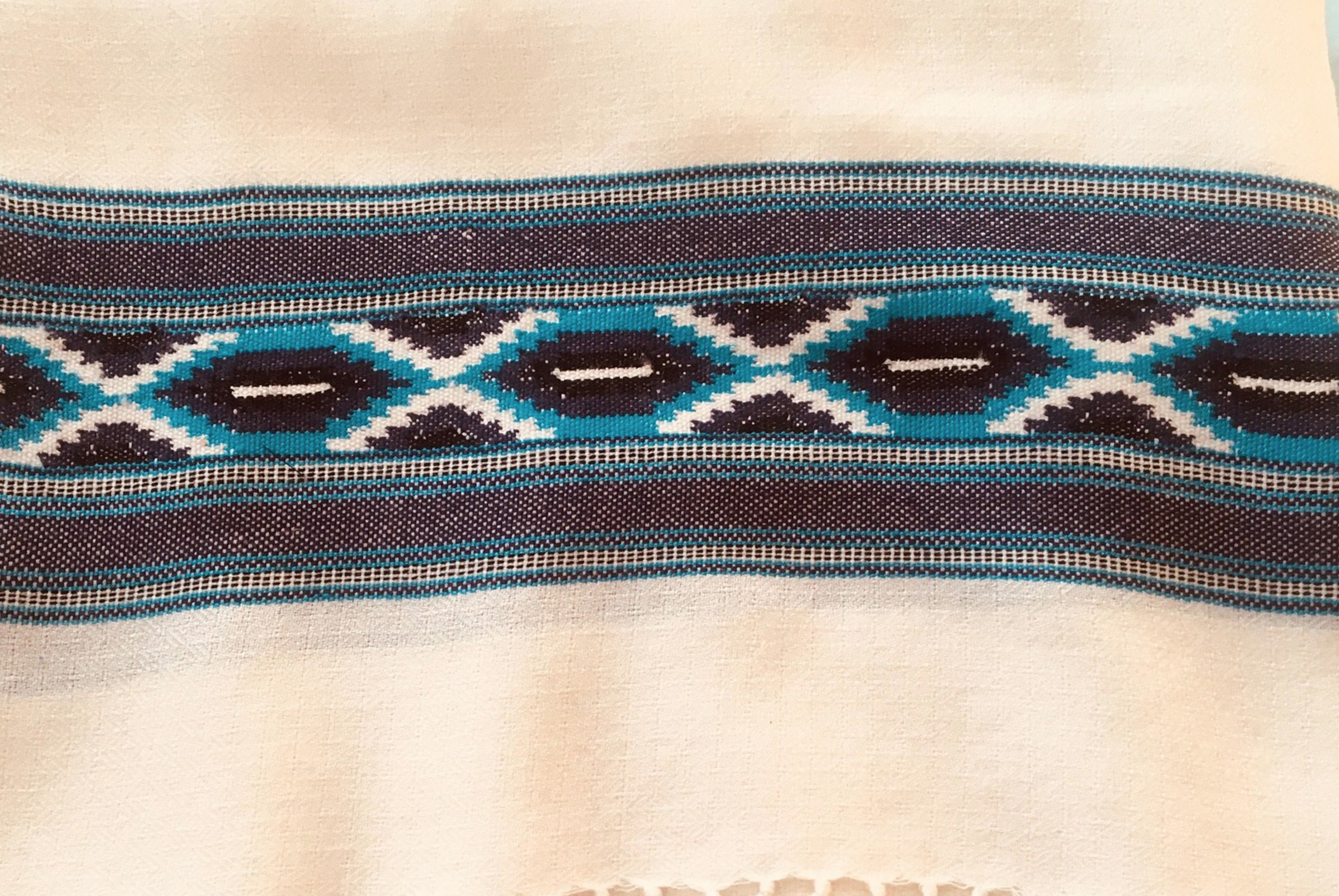 Close-up of the Swatantra ethnic meditation shawl featuring intricate turquoise and navy geometric patterns on a cream background.