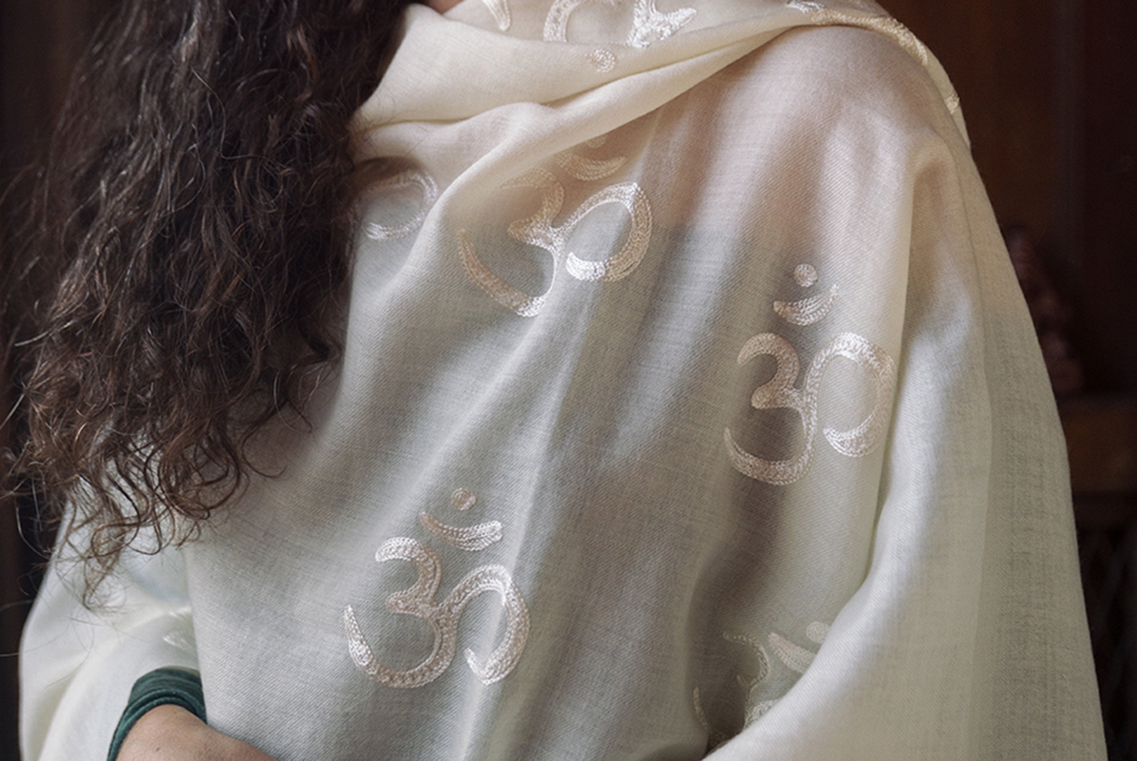 Detailed shot of white shawl showing Om symbols against a wooden background.