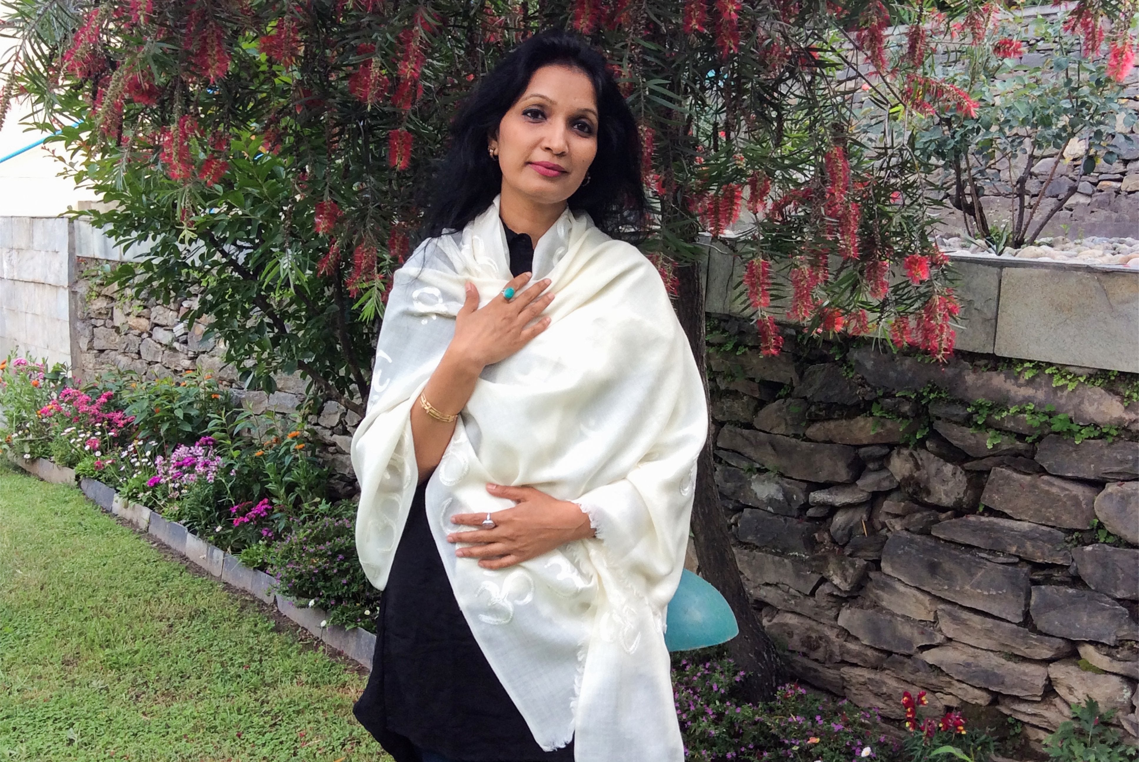 Woman in a white shawl in a garden with red flowers in the background.