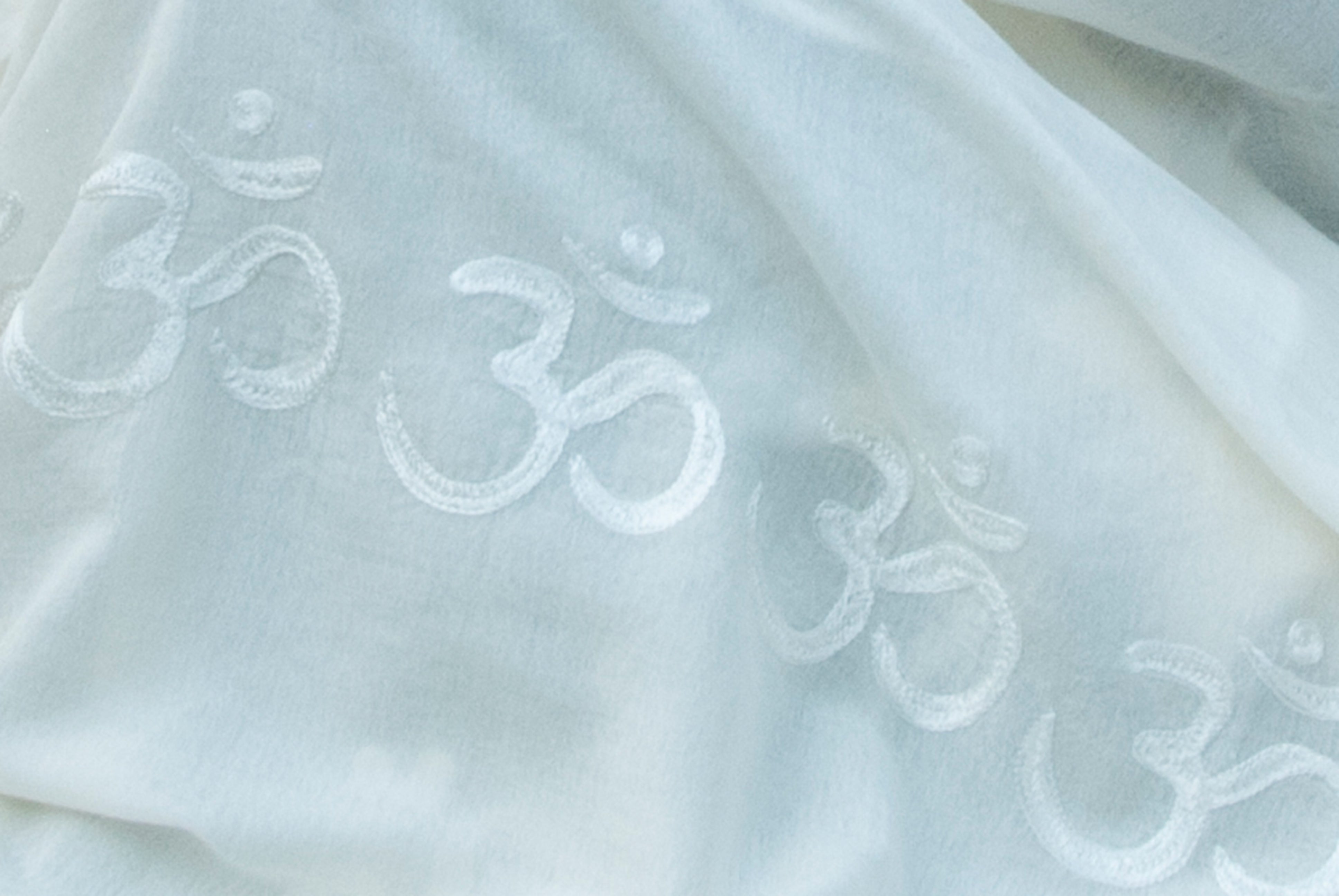 Close-up of a white shawl showing embroidered Om symbols, focusing on the intricate details of the fabric.