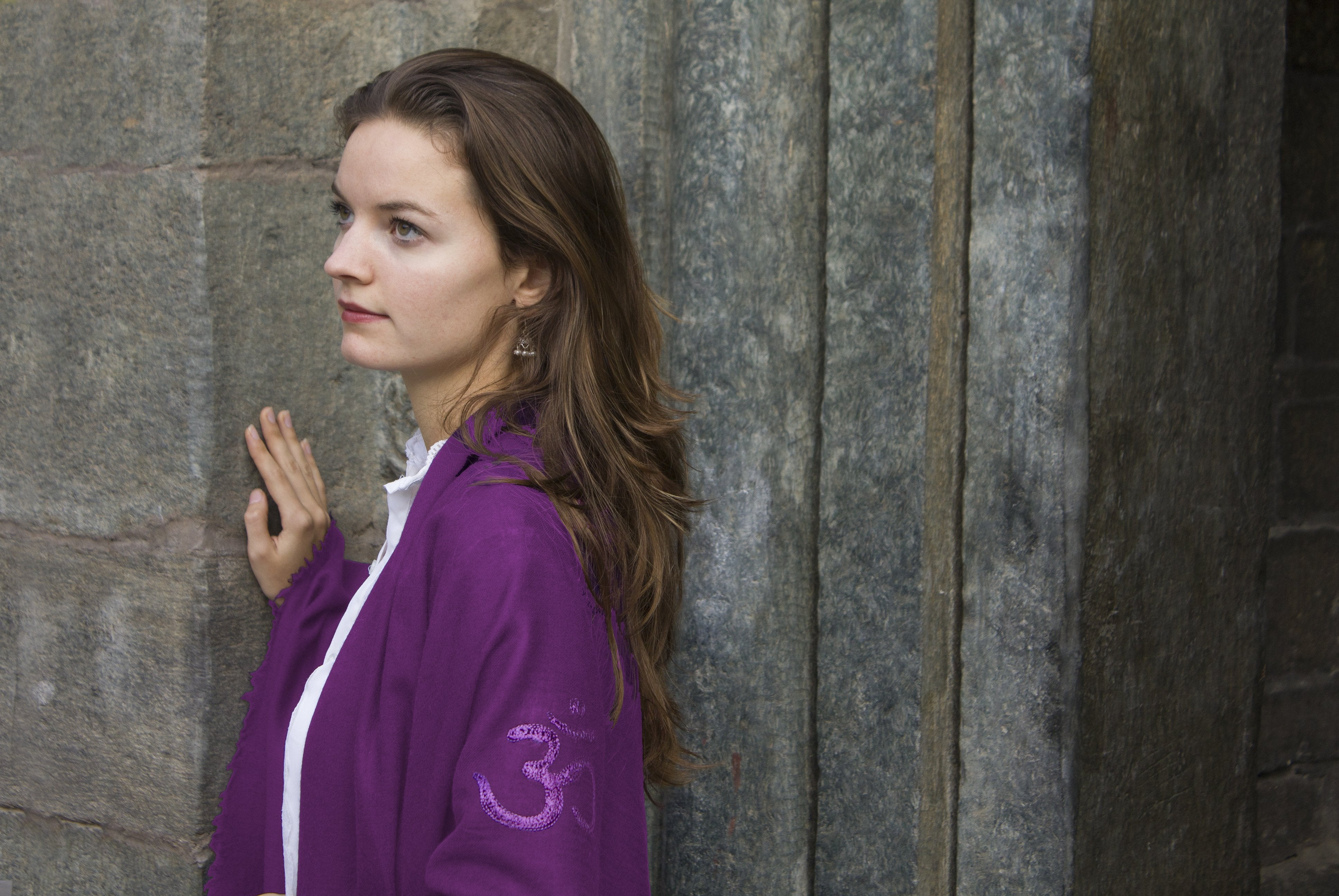 Side view of woman in purple shawl with temple stone walls.